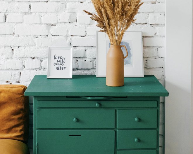 A green dresser with two picture on it and a flower vase